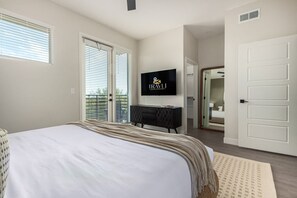 Un dormitorio con cama, televisión montada en la pared, cómoda y puerta que da a otra habitación.