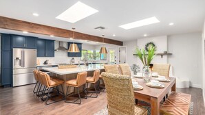 A modern kitchen with dark blue cabinets, a central island, and a dining area with wicker chairs and a wooden table.