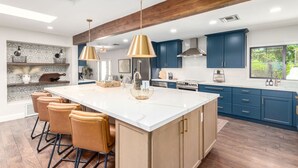 A modern kitchen with a large island, bar stools, blue cabinets, and pendant lighting.