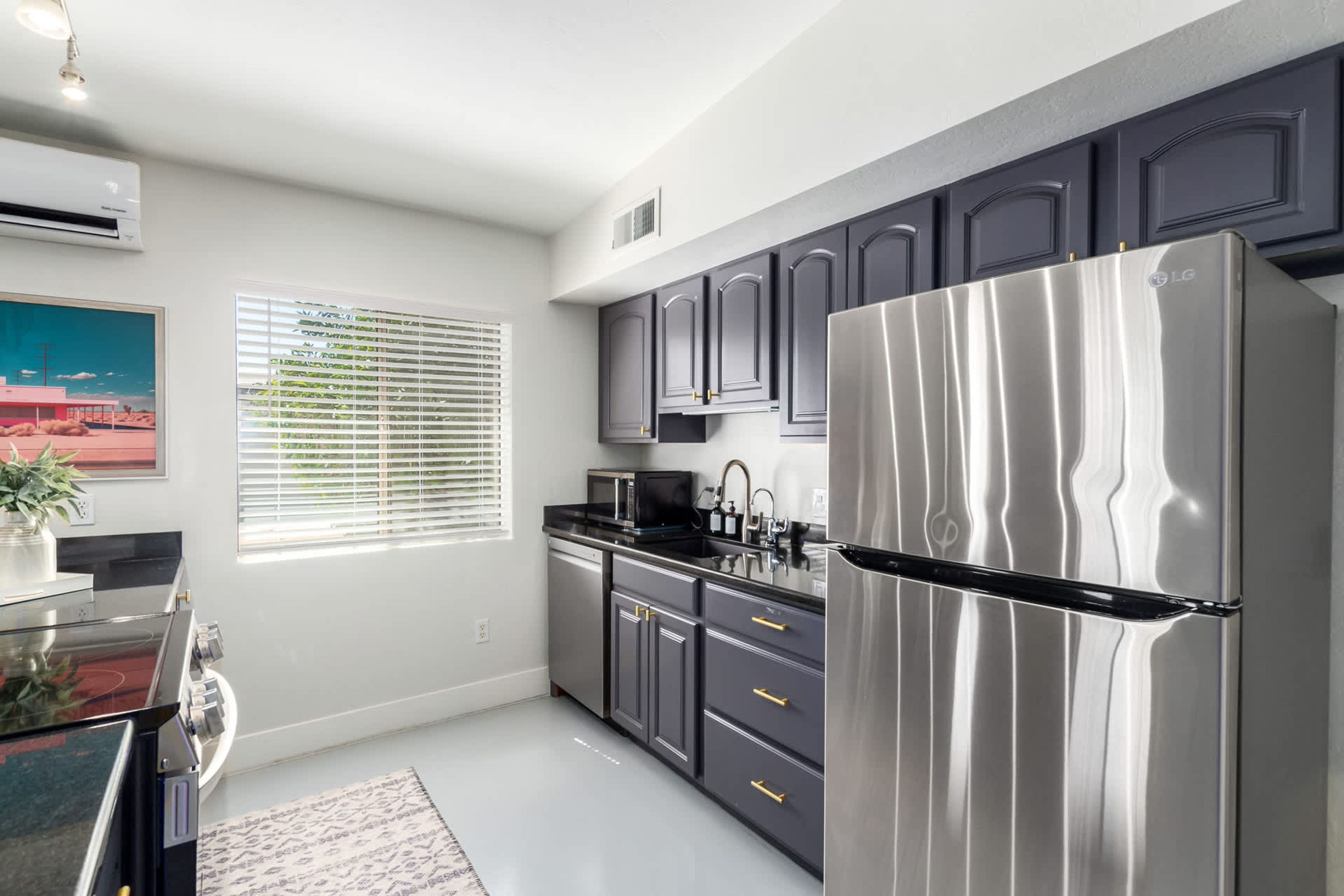 A modern kitchen with stainless steel appliances, grey cabinets, and a window with blinds.