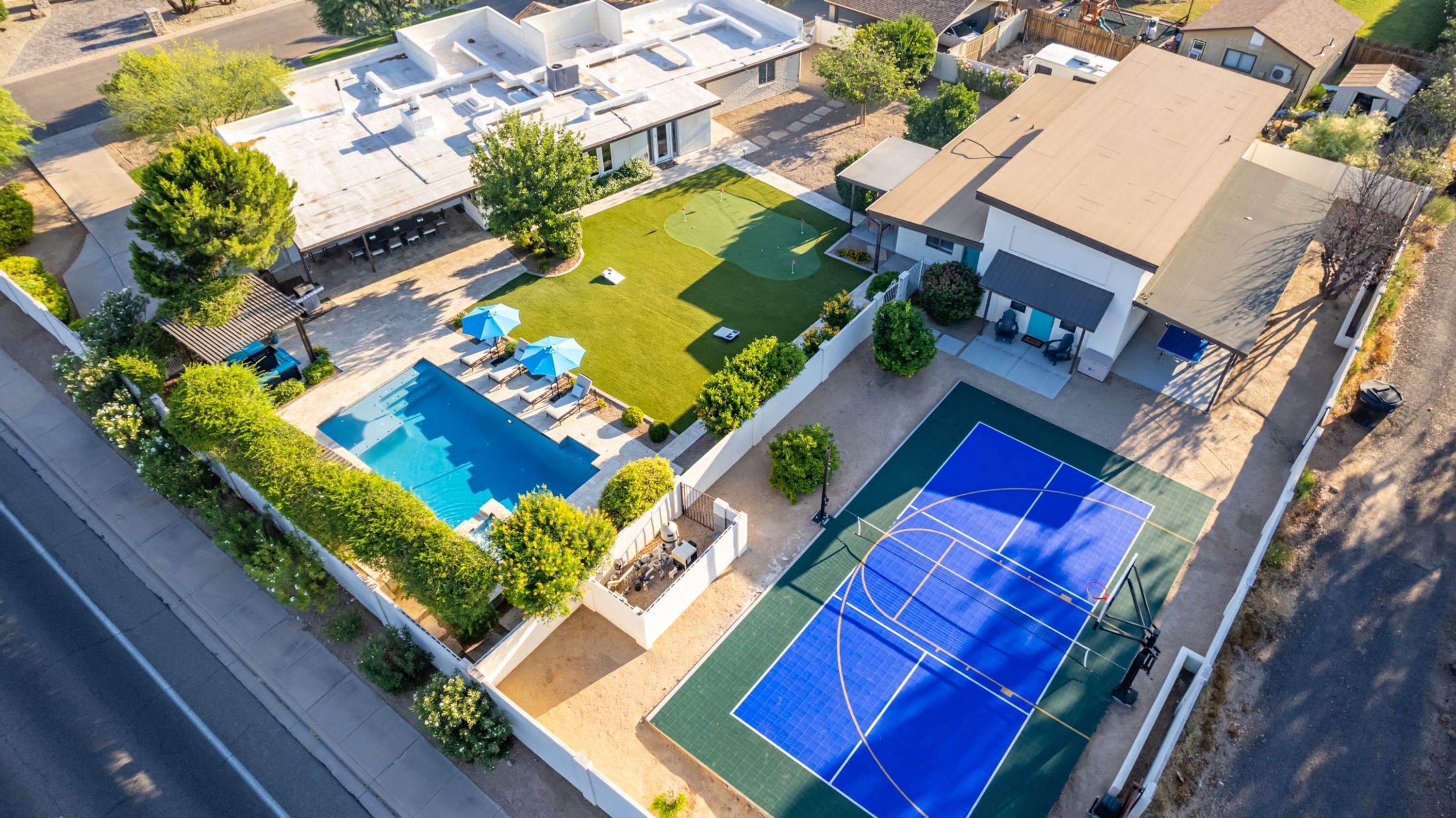 Vista aérea de una propiedad residencial con piscina, cancha de tenis y jardín ajardinado.