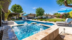 A swimming pool with a water feature, surrounded by lounge chairs and umbrellas, with a clear sky above.