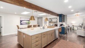 A spacious kitchen with a large island, wooden beams on the ceiling, pendant lighting, and a view into the dining area.