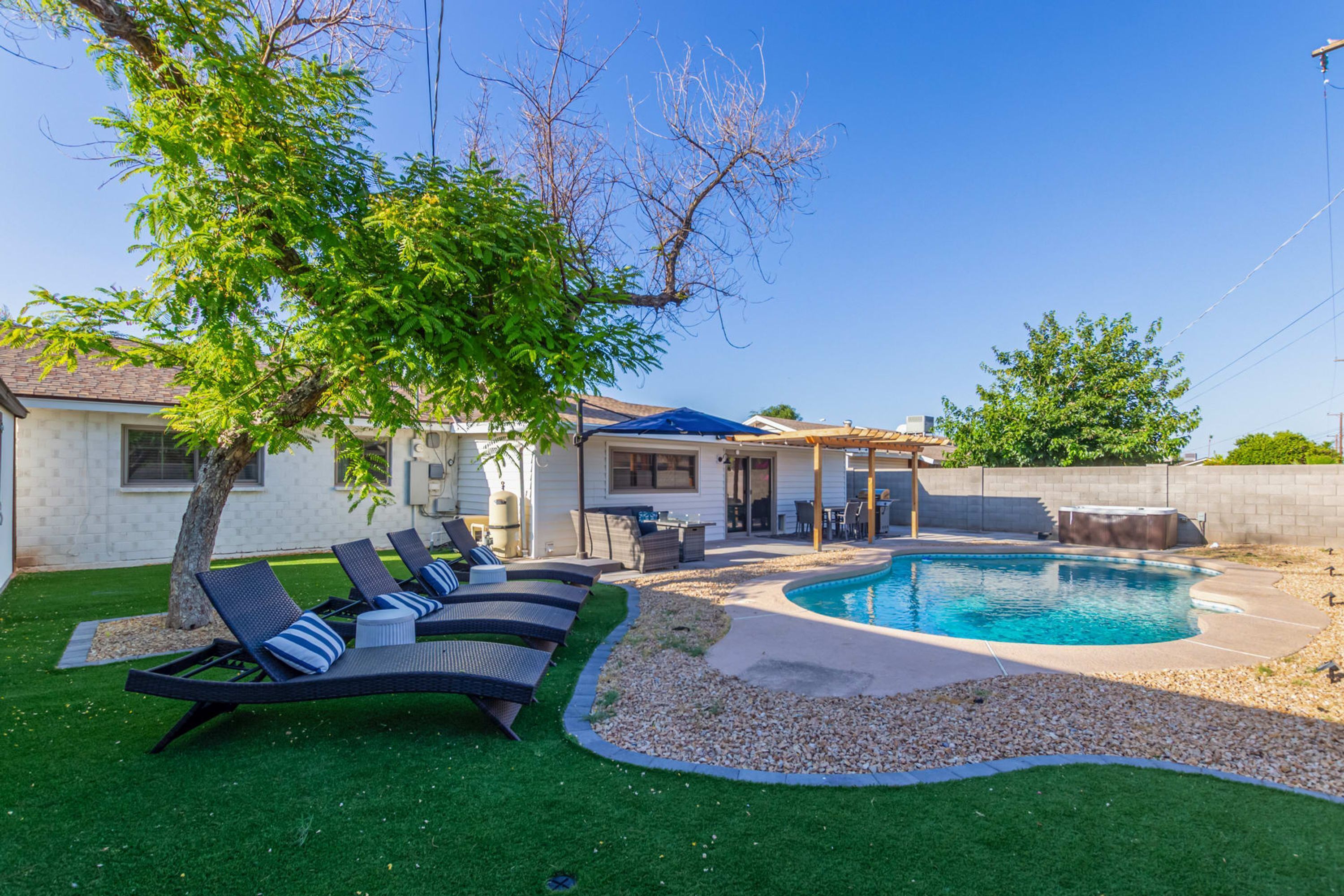 A backyard with a swimming pool, lounge chairs, a tree, and a patio area.