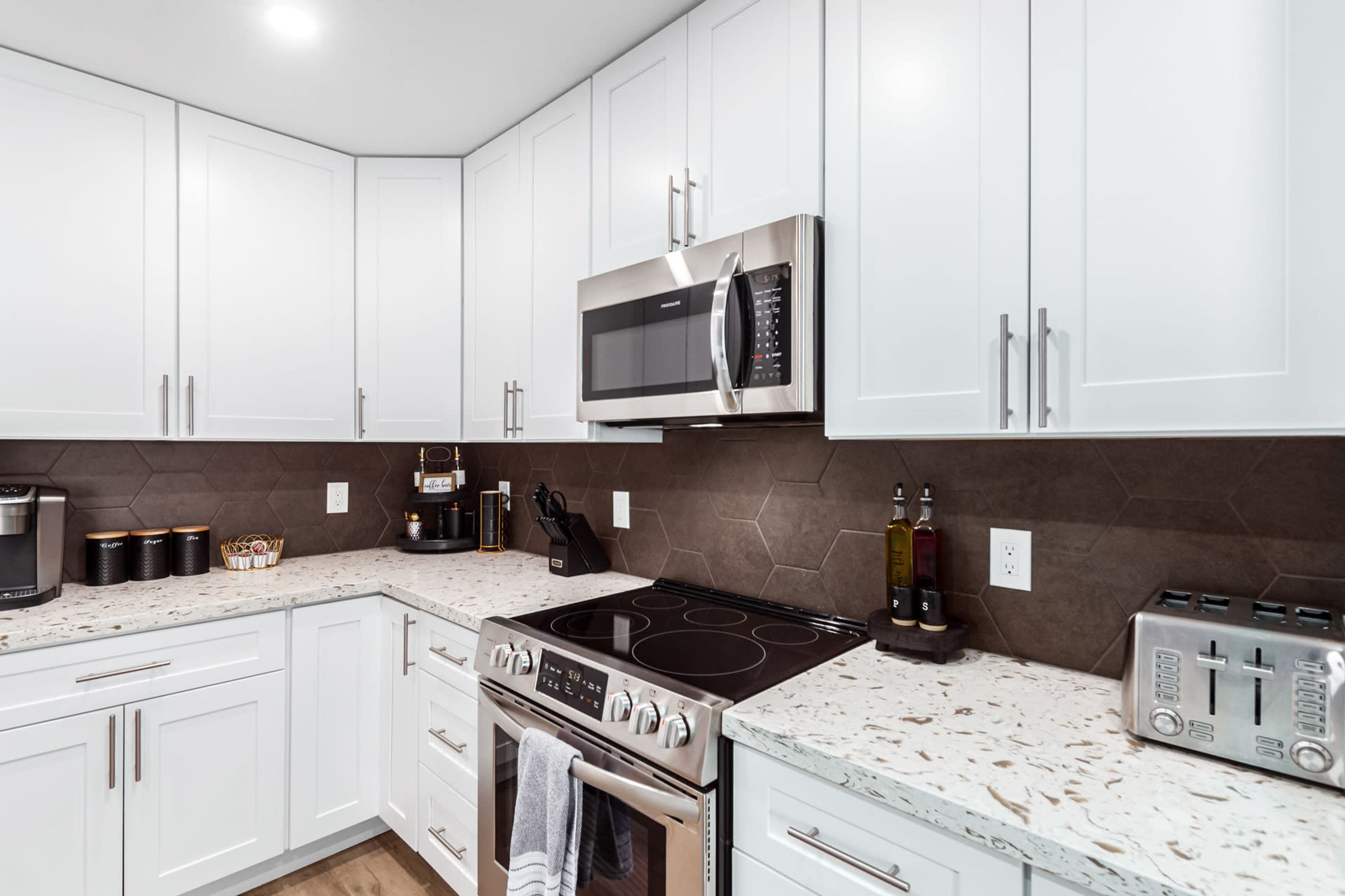 A modern kitchen with white cabinets, a stainless steel microwave, a gas stove, and a toaster.