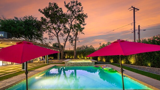 A swimming pool with two red umbrellas, lounge chairs, and a stone hot tub.