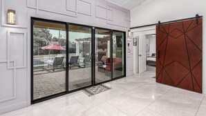A modern interior with a sliding glass door leading to an outdoor patio area, a large mirror, and a geometric-patterned sliding door.