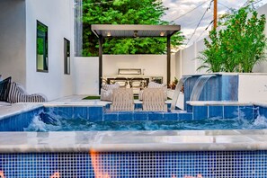 Un área de piscina moderna al aire libre con un jacuzzi, sillones de descanso y una pérgola.