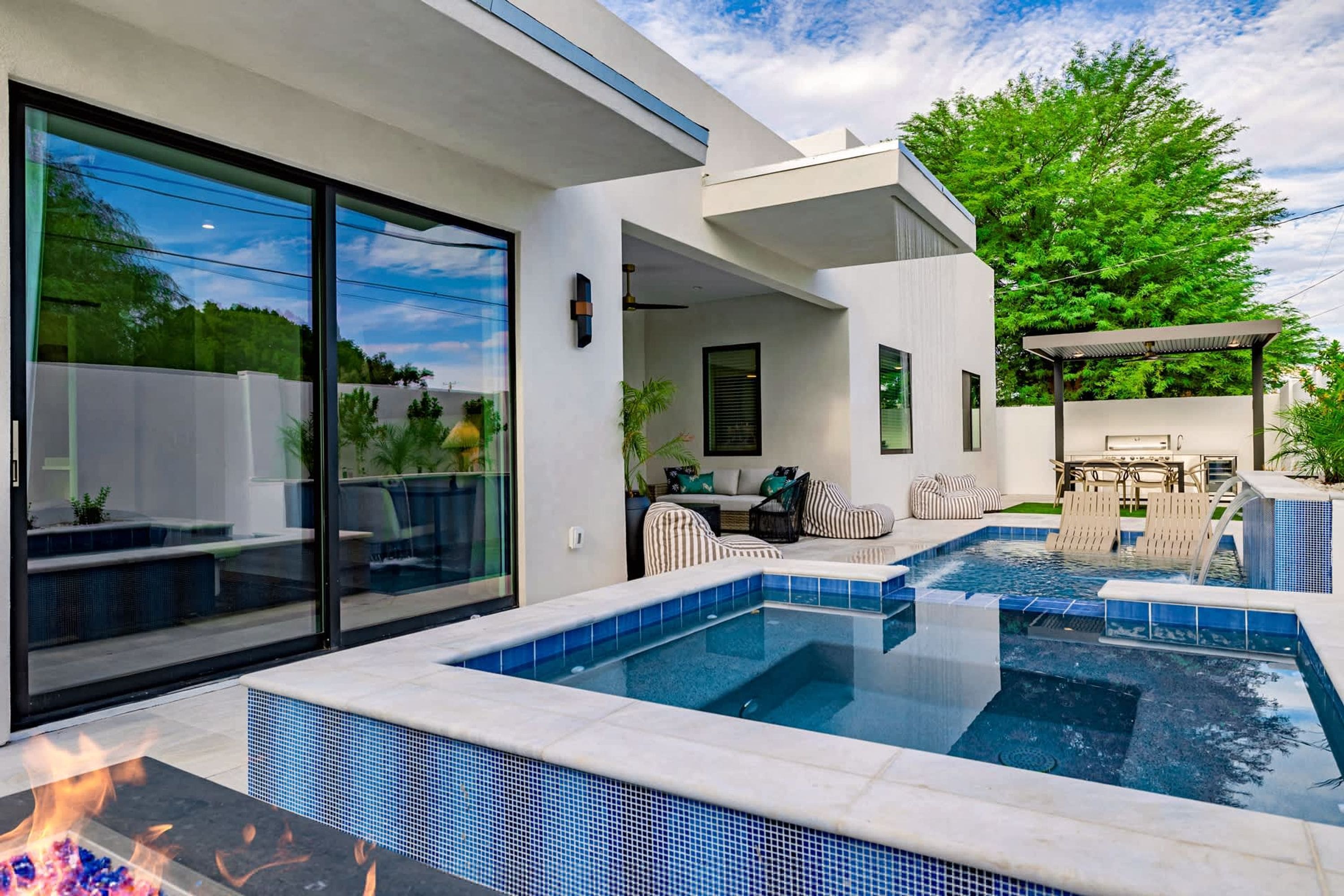 A modern outdoor pool area with a fire feature, a covered seating area, and a patio with outdoor furniture.