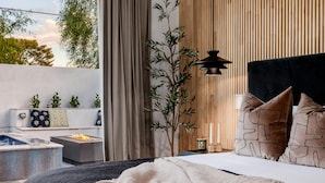 A modern bedroom with a bed, bedside table, and a view of the outdoors. - The Carlisle Experience 4 Showers Heated Pool (Scottsdale)