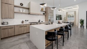 A modern kitchen with a central island, wooden cabinets, and pendant lighting. - The Carlisle Experience 4 Showers Heated Pool (Scottsdale)