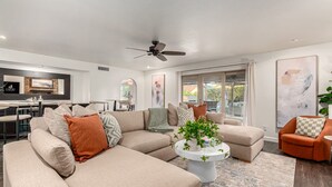 A modern living room with a sectional sofa, a coffee table, and a dining area in the background. - Spanish Wells Retreat Free Pool Heat Spa BBQ (Scottsdale)