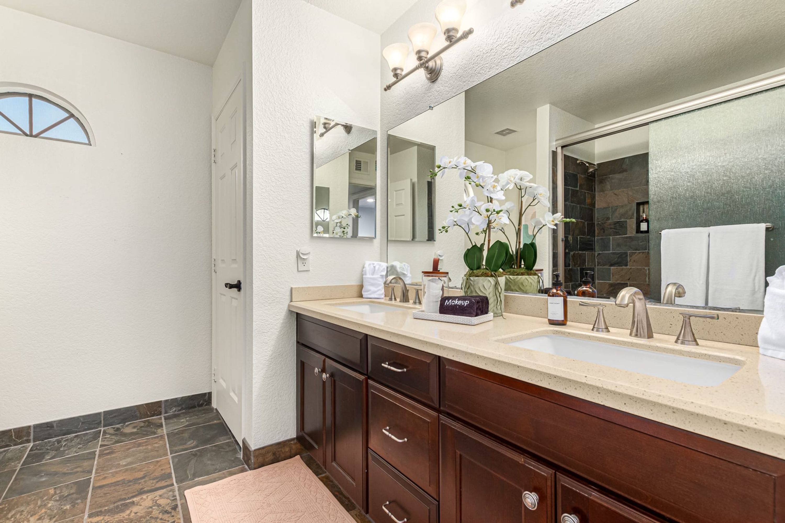 A bathroom with a double sink vanity, a large mirror, and a shower area.