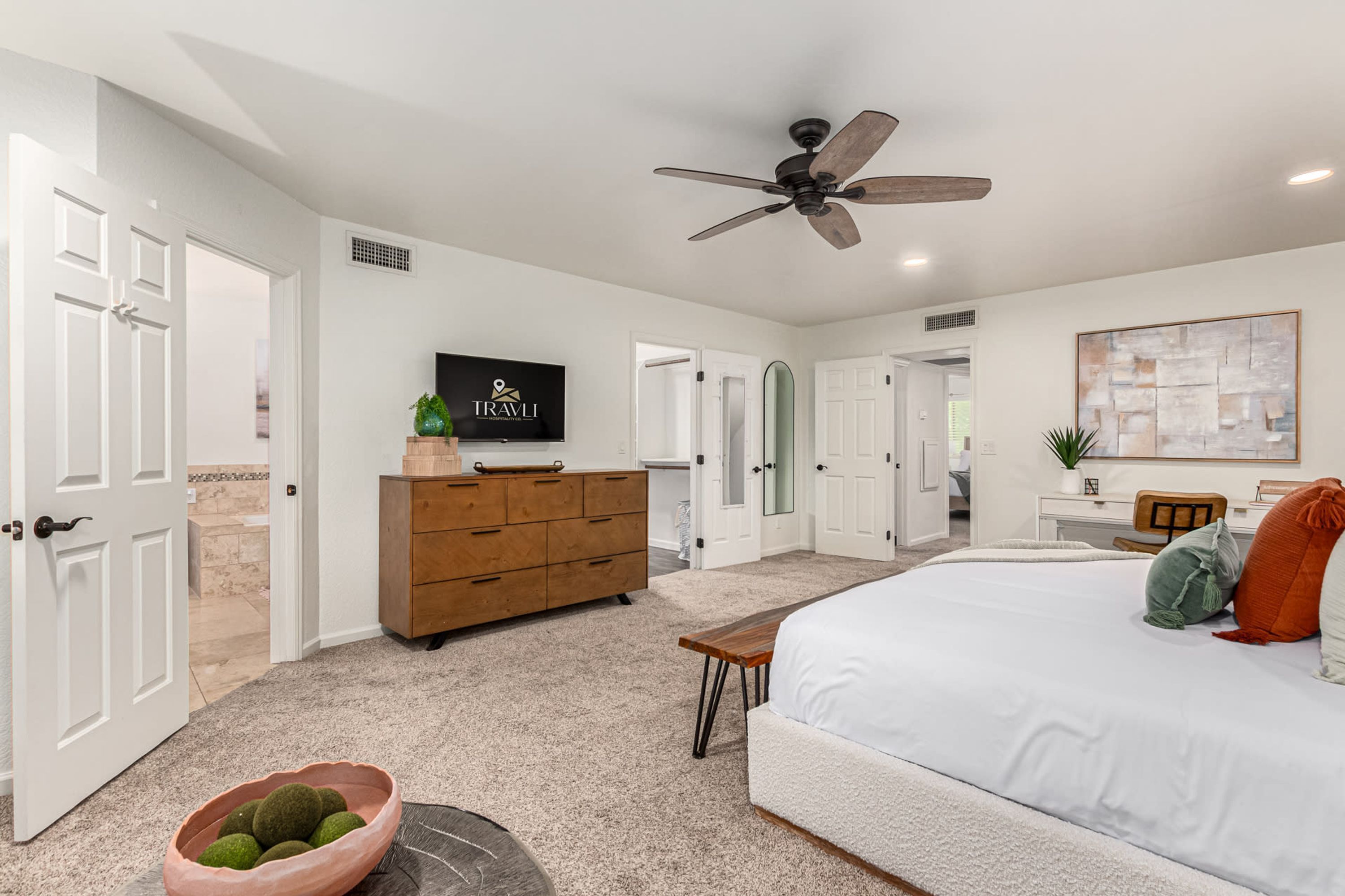 Une chambre à coucher avec un grand lit, un ventilateur de plafond, une commode, un téléviseur et un bureau avec une chaise.