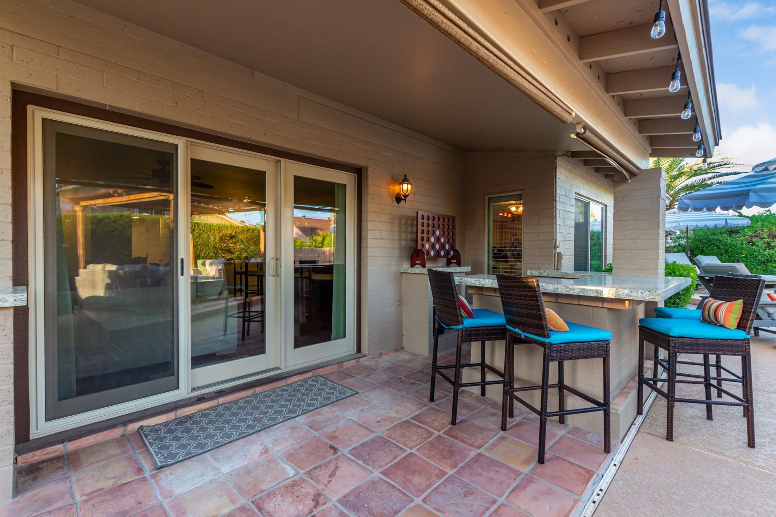 A patio area with a bar, two wicker chairs with cushions, and a sliding glass door leading to a covered outdoor space.