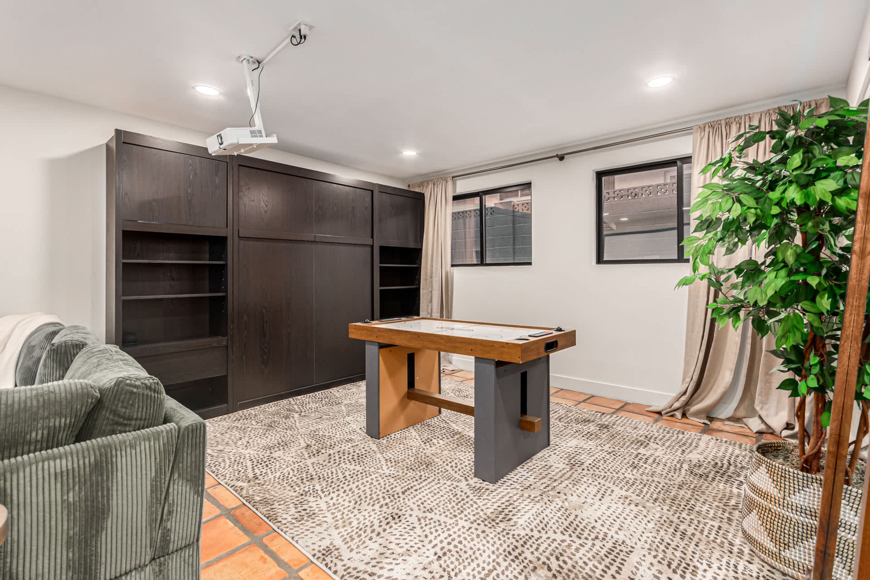A room with a pool table, dark wooden cabinets, a green sofa, and a large potted plant.