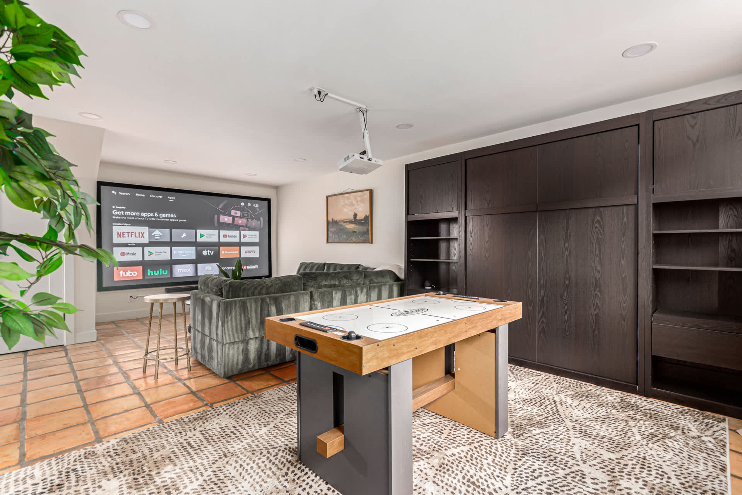 A modern living room with a foosball table, a large flat-screen TV, a sofa, and dark wooden shelving.