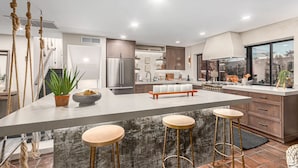 A modern kitchen with a central island, bar stools, and hanging ropes.
