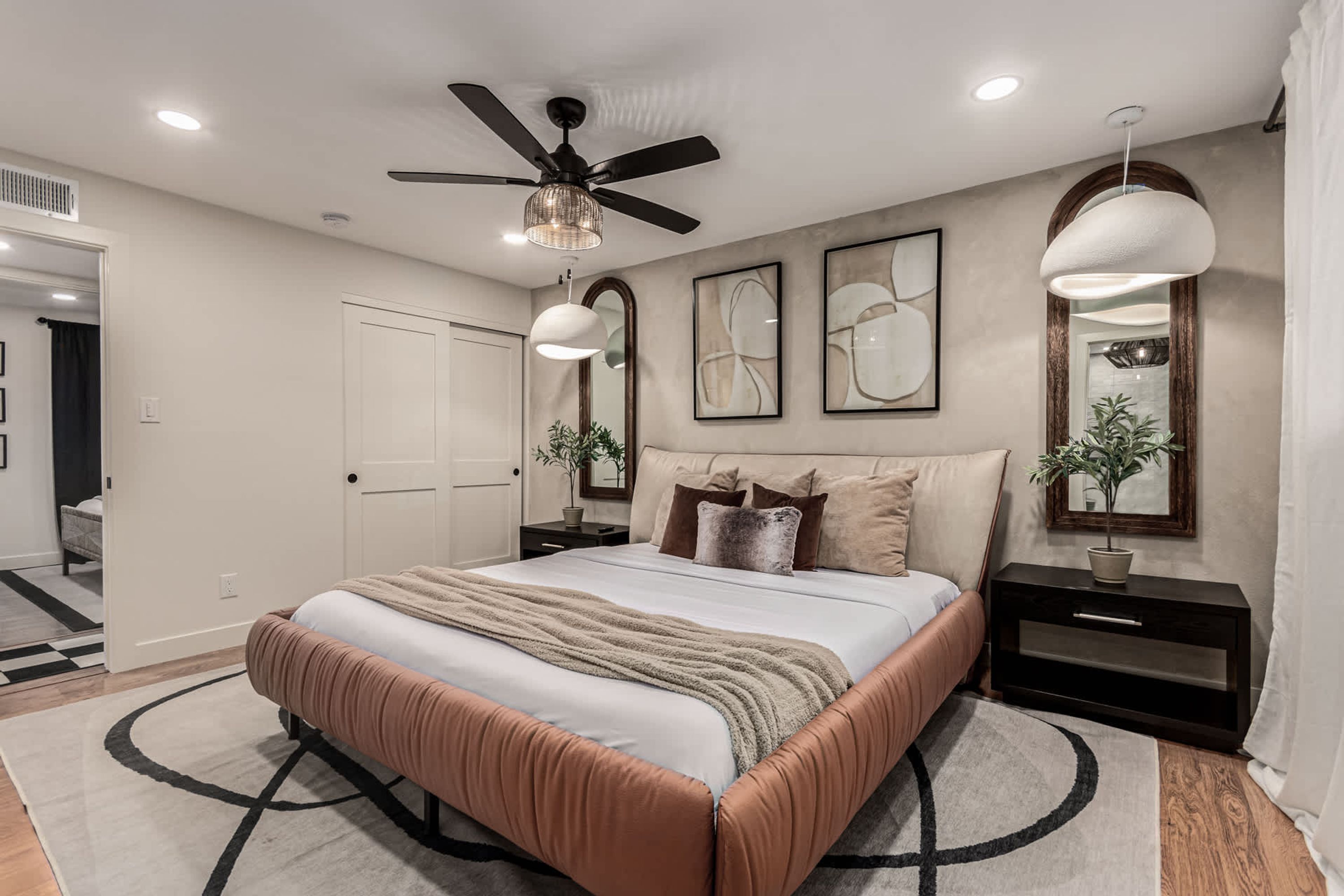 A bedroom with a bed, ceiling fan, pendant lights, and a large mirror.