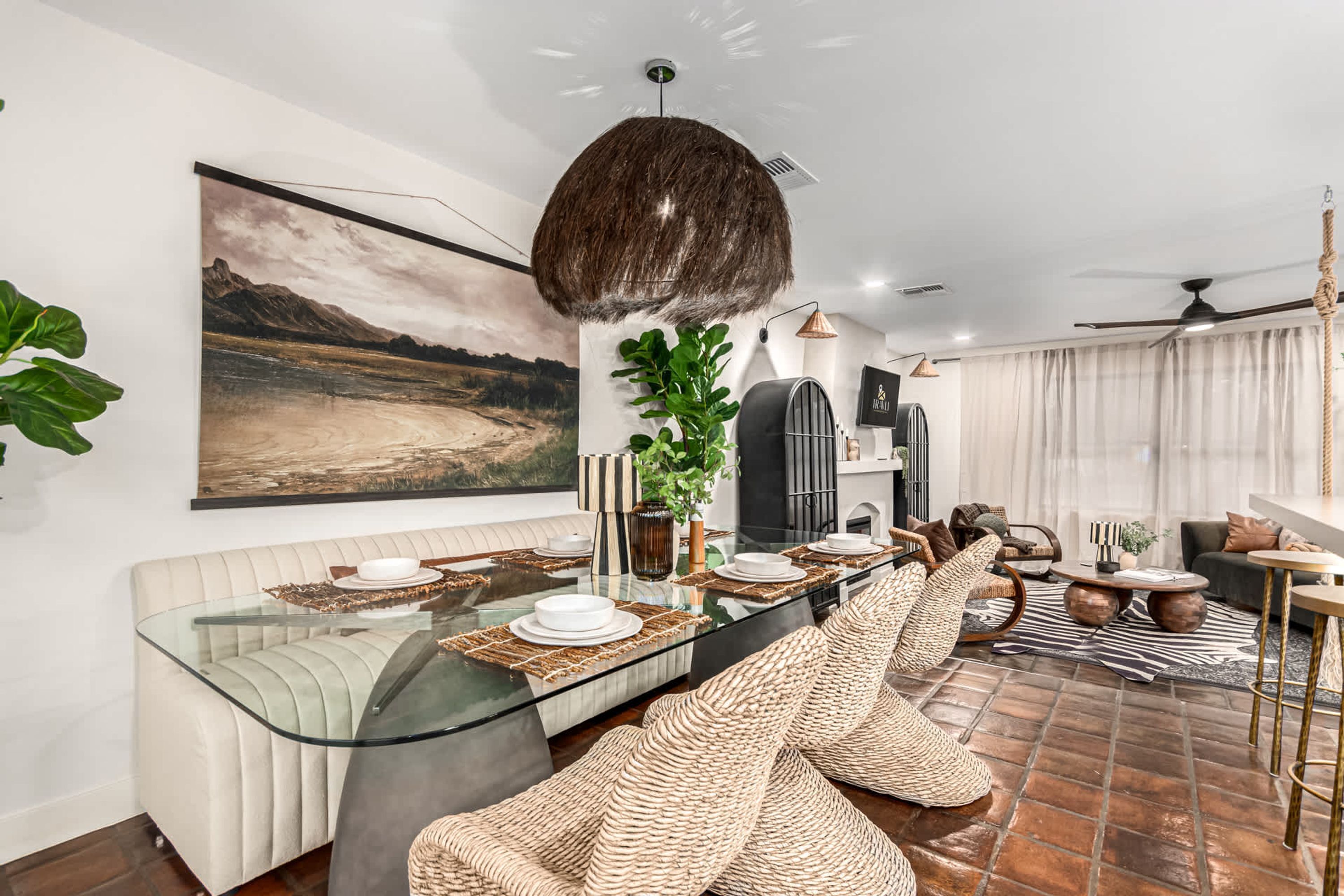 Un comedor moderno con una mesa de vidrio, asientos acolchados y un cuadro grande con un paisaje en la pared.
