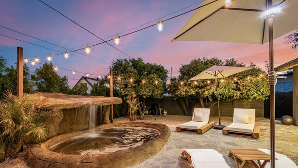 A serene outdoor setting with a hot tub, lounge chairs, and string lights against a twilight sky.