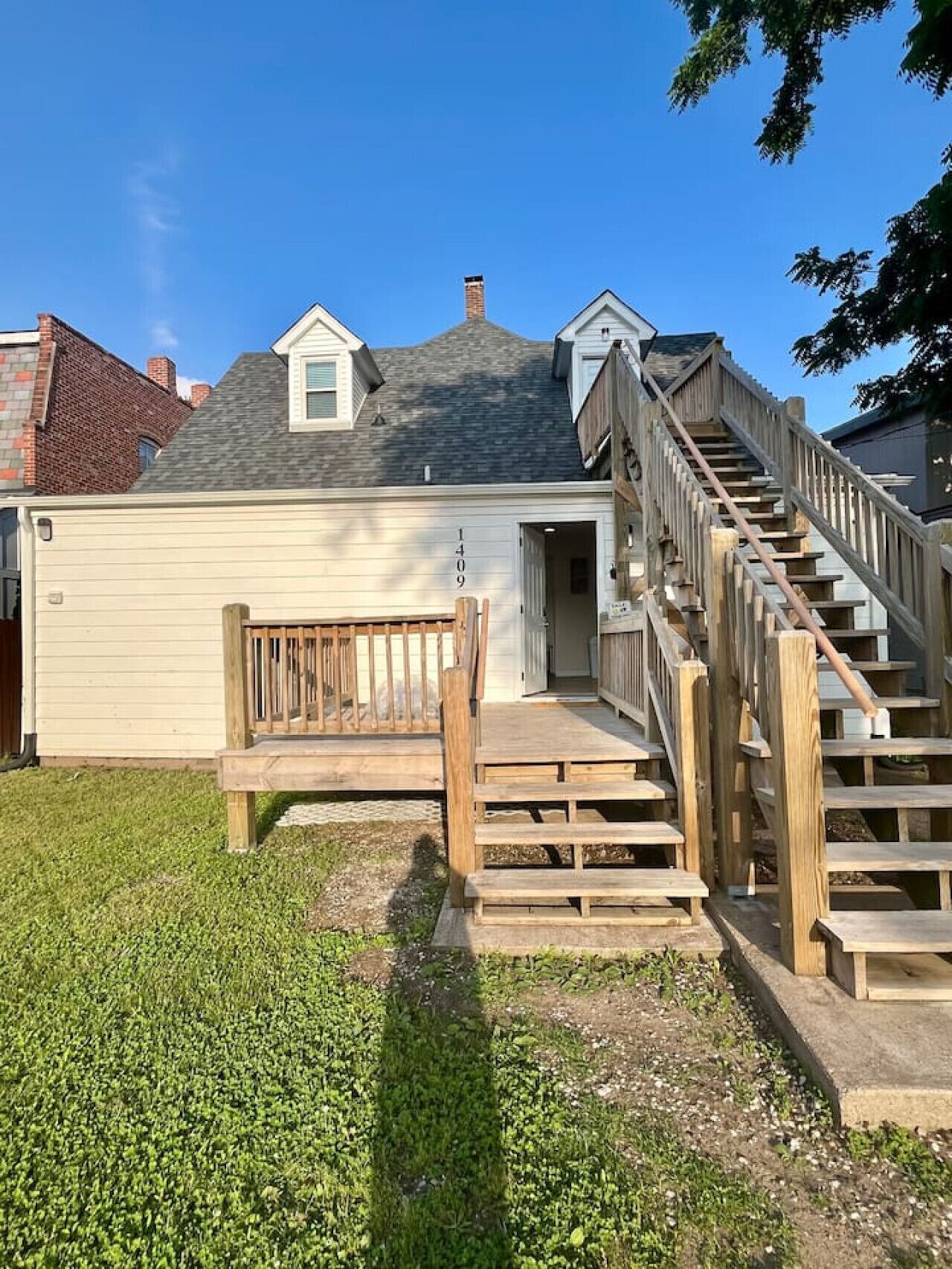 A residential house with a wooden staircase leading to a garage, a small porch, and a clear sky.