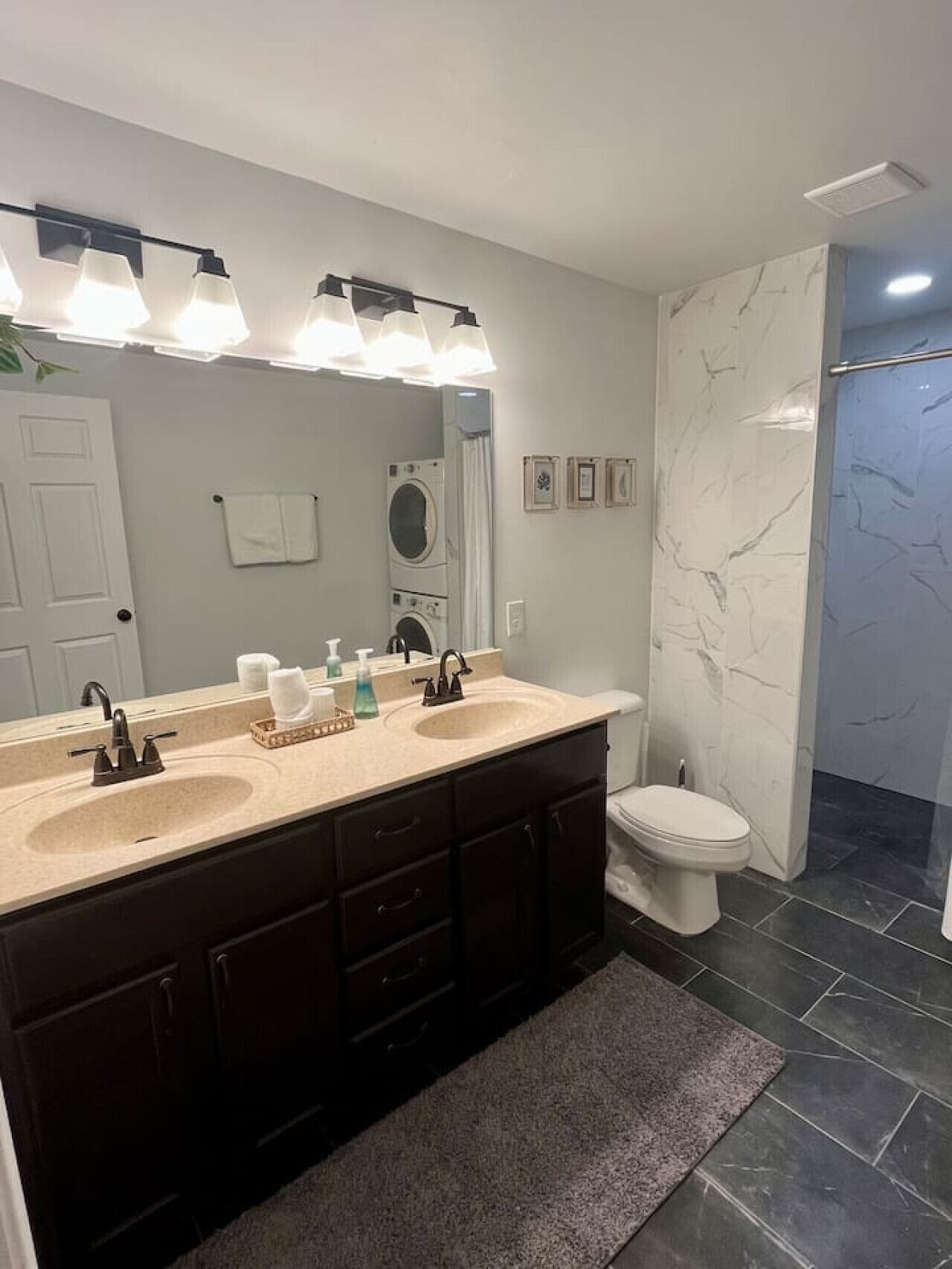 Une salle de bain moderne avec un meuble-lavabo à deux vasques, des toilettes, une douche et un grand miroir avec un éclairage situé au-dessus.