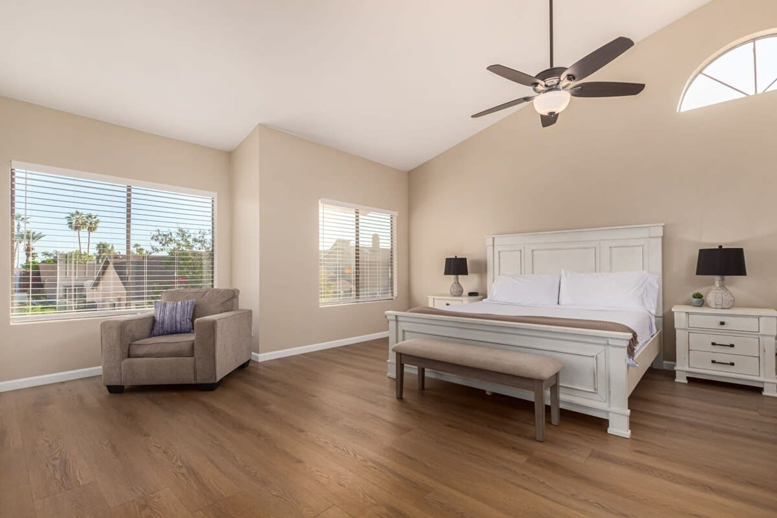 A bedroom with a bed, a chair, a bench, a nightstand, and a ceiling fan.