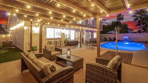 An outdoor patio area with wicker furniture, string lights, and a pool.