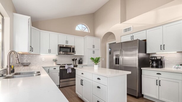 A modern kitchen with white cabinetry, stainless steel appliances, and a large island.