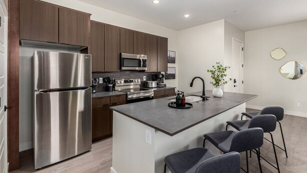 A modern kitchen with stainless steel appliances, a central island with bar stools, and dark wood cabinetry. - Macallister 1008 Close to Golf Htd Pool BBQ (Scottsdale)