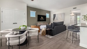A modern living room with a grey sofa, a dining table with chairs, a TV mounted on the wall, and a ceiling fan. - Macallister 1008 Close to Golf Htd Pool BBQ (Scottsdale)