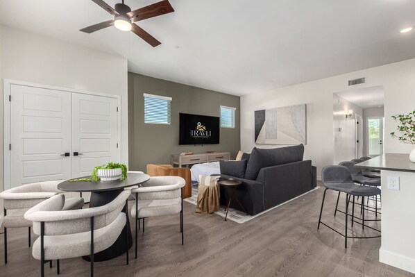 A modern living room with a grey sofa, a dining table with chairs, a TV mounted on the wall, and a ceiling fan. - Macallister 1008 Close to Golf Htd Pool BBQ (Scottsdale)