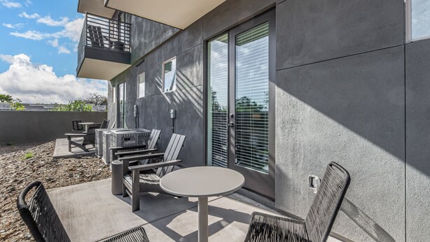 Un patio esterno con un tavolo rotondo e sedie, una zona relax con tavolo e sedute, e un balcone con ringhiera.