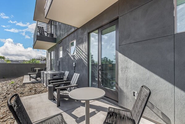 Een buitenterras met een ronde tafel en stoelen, een klein zithoekje met een tafel en stoelen, en een balkon met een hekwerk.