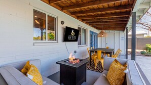 An outdoor patio with a fire pit, a sofa, and yellow chairs. - Desert Diamond Oasis Private Pool Bar Games (Scottsdale)