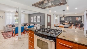 A modern kitchen with a central island, stainless steel range hood, and a dining area with a table and chairs. - Desert Diamond Oasis Private Pool Bar Games (Scottsdale)
