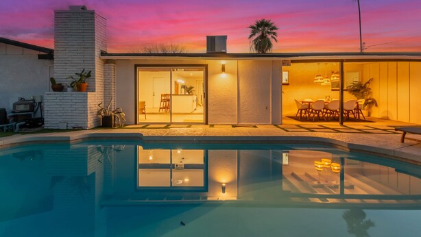 Ett modernt hus med en swimmingpool, en uteplats med utemöbler och en solnedgångshimel.