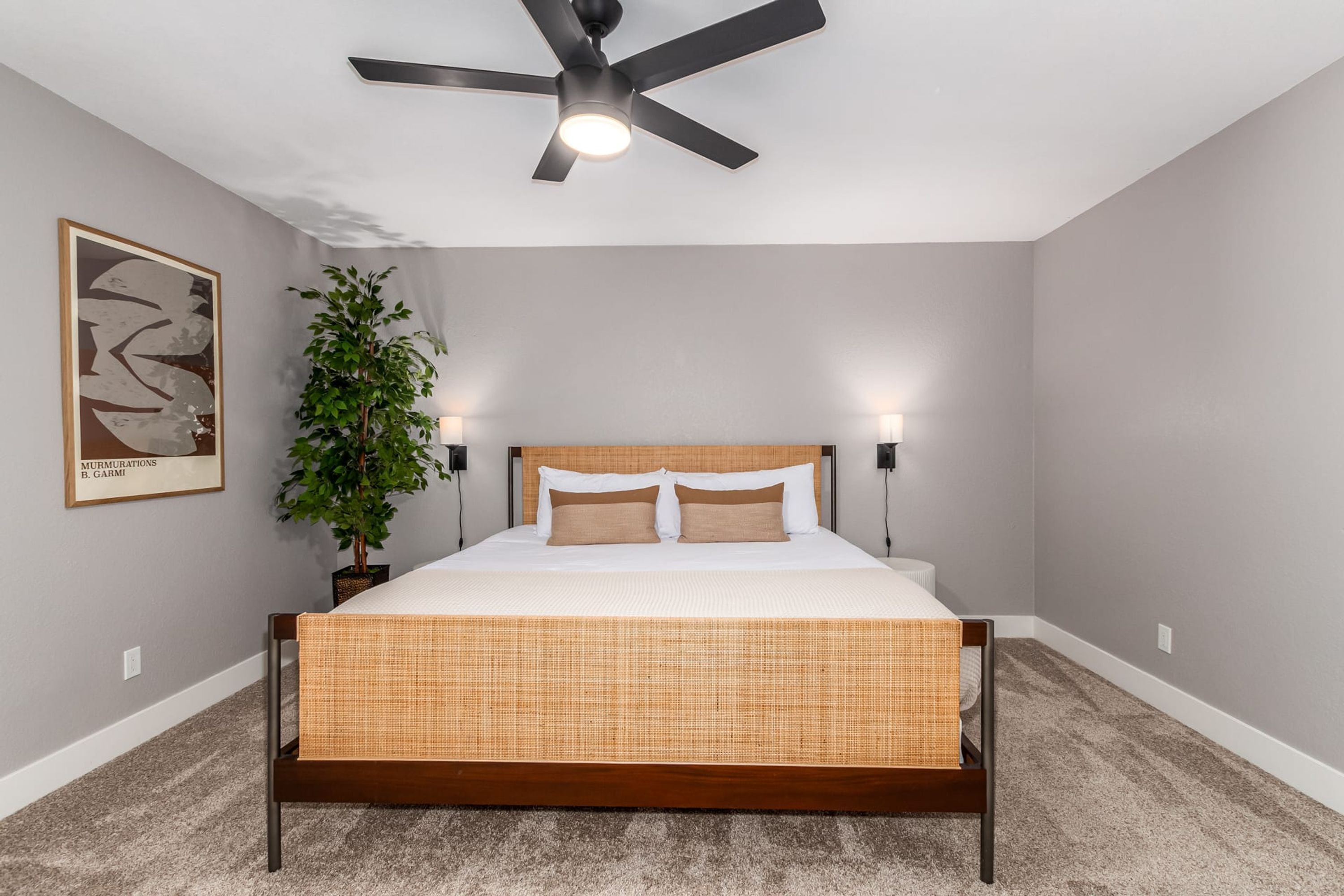 Une chambre à coucher avec un lit, un ventilateur de plafond, des lampes fixées au mur et une plante en pot.