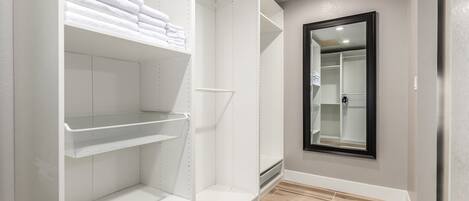 A walk-in closet with white shelving units, a mirror, and a wooden floor.