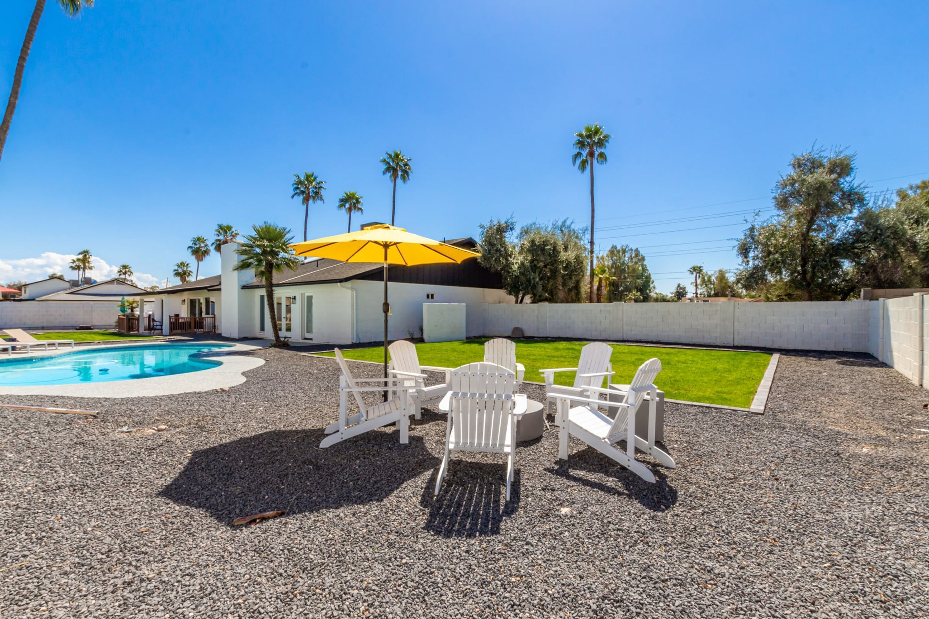 A pool area with a yellow umbrella, white Adirondack chairs, and a small table.