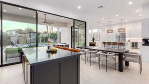A modern kitchen with a large island, dining area with chairs, and a view of a swimming pool. - Anderson LUX Estate Private Bar Pool Sleeps 12 (Scottsdale)
