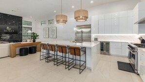 A modern kitchen with white cabinets, a stainless steel refrigerator, a built-in oven, and a bar area with stools. - Anderson LUX Estate Private Bar Pool Sleeps 12 (Scottsdale)