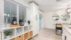 A modern kitchen with white cabinetry, a coffee station, and a dining area with a table and chairs. - Desert Rose Retreat Heated Pool 2 Masters Gameroom (Scottsdale)