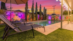 A poolside area with lounge chairs and an umbrella, surrounded by a decorative wall with floral patterns. - Desert Rose Retreat Heated Pool 2 Masters Gameroom (Scottsdale)