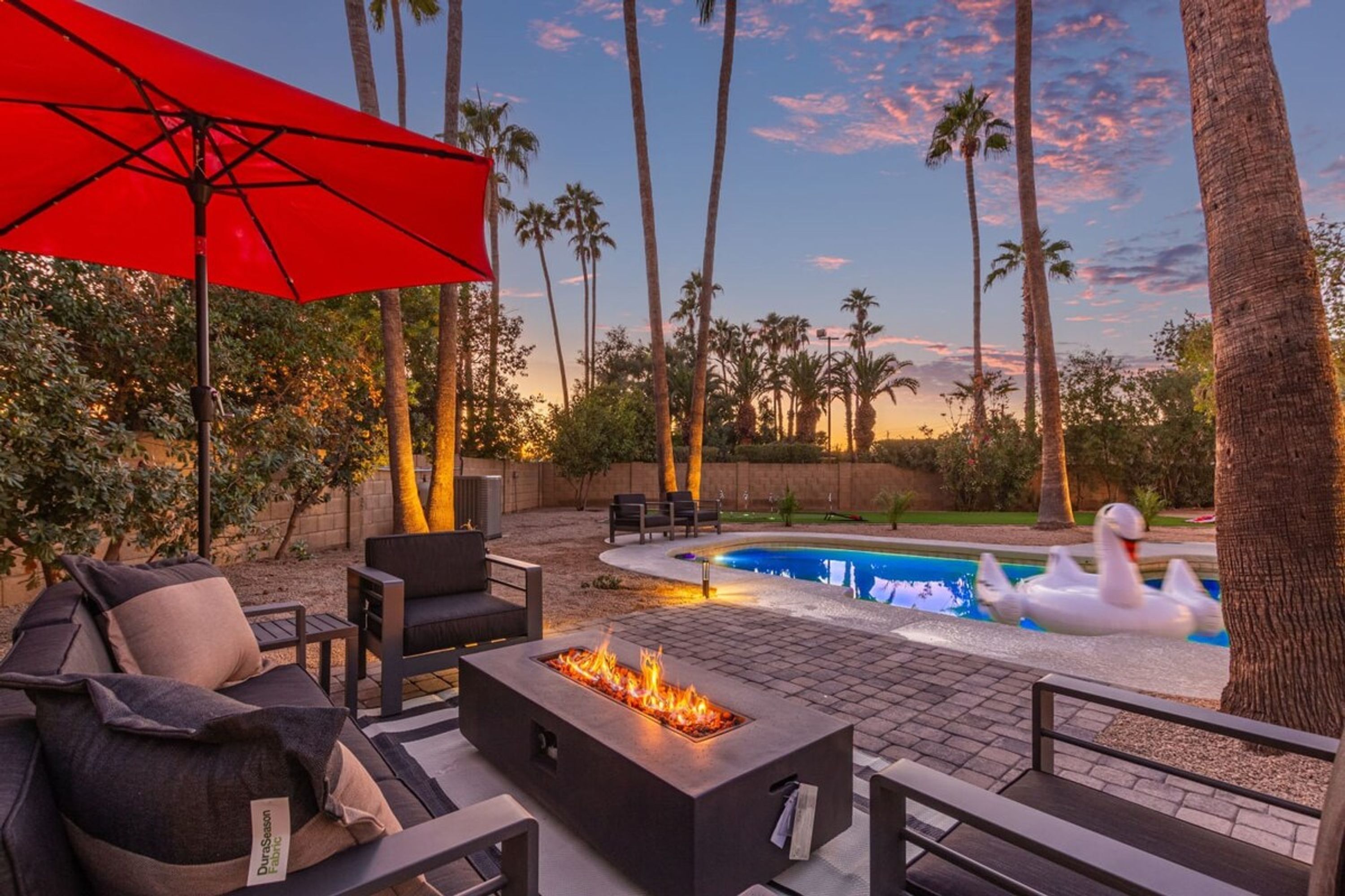 Un espace patio aménagé avec un foyer extérieur, du mobilier de jardin et une piscine agrémentée d’un flotteur en forme de cygne.