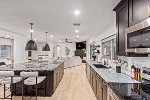 A modern kitchen with a large island, dark cabinetry, and stainless steel appliances. - Doce Palmas Free Htd Pool Spa Putt Grn (Scottsdale)