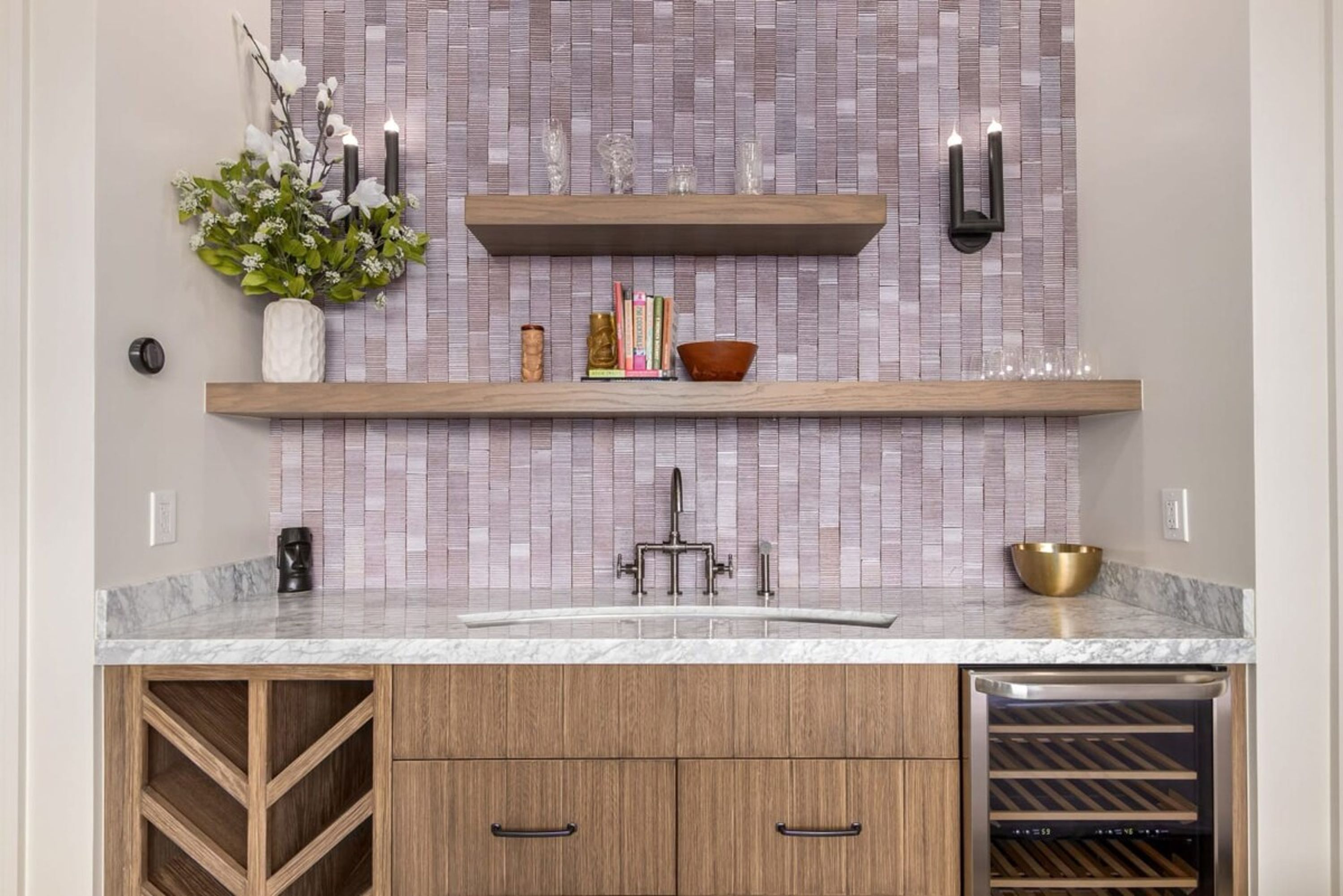 A kitchen with a marble countertop, wooden cabinets, a wine cooler, and a tiled backsplash.