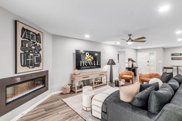 A modern living room with a fireplace, a large flat-screen TV, a sofa, and a ceiling fan. - The Monterey Resort Style Pickleball Pool Putt (Scottsdale)