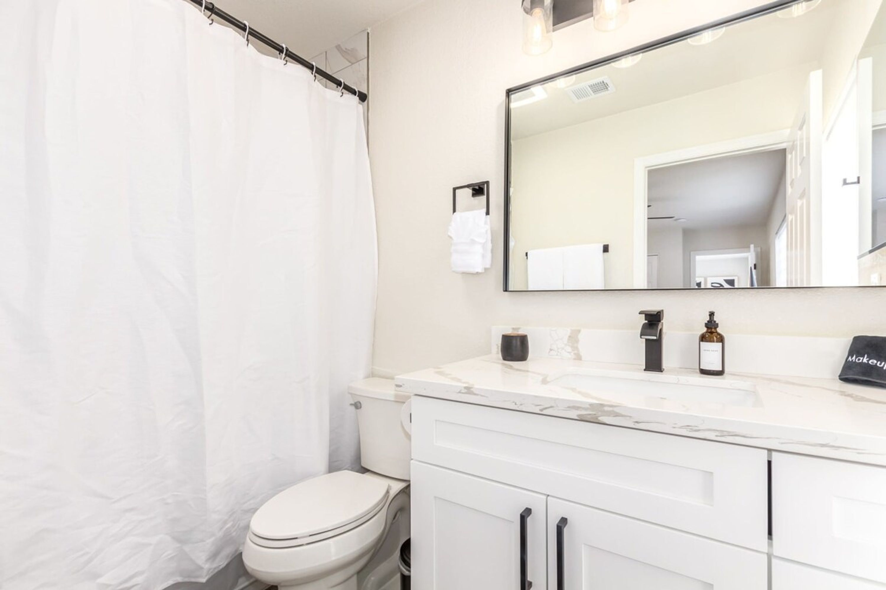 Une salle de bain moderne avec des toilettes blanches, un grand miroir et un meuble-lavabo blanc doté de tiroirs.